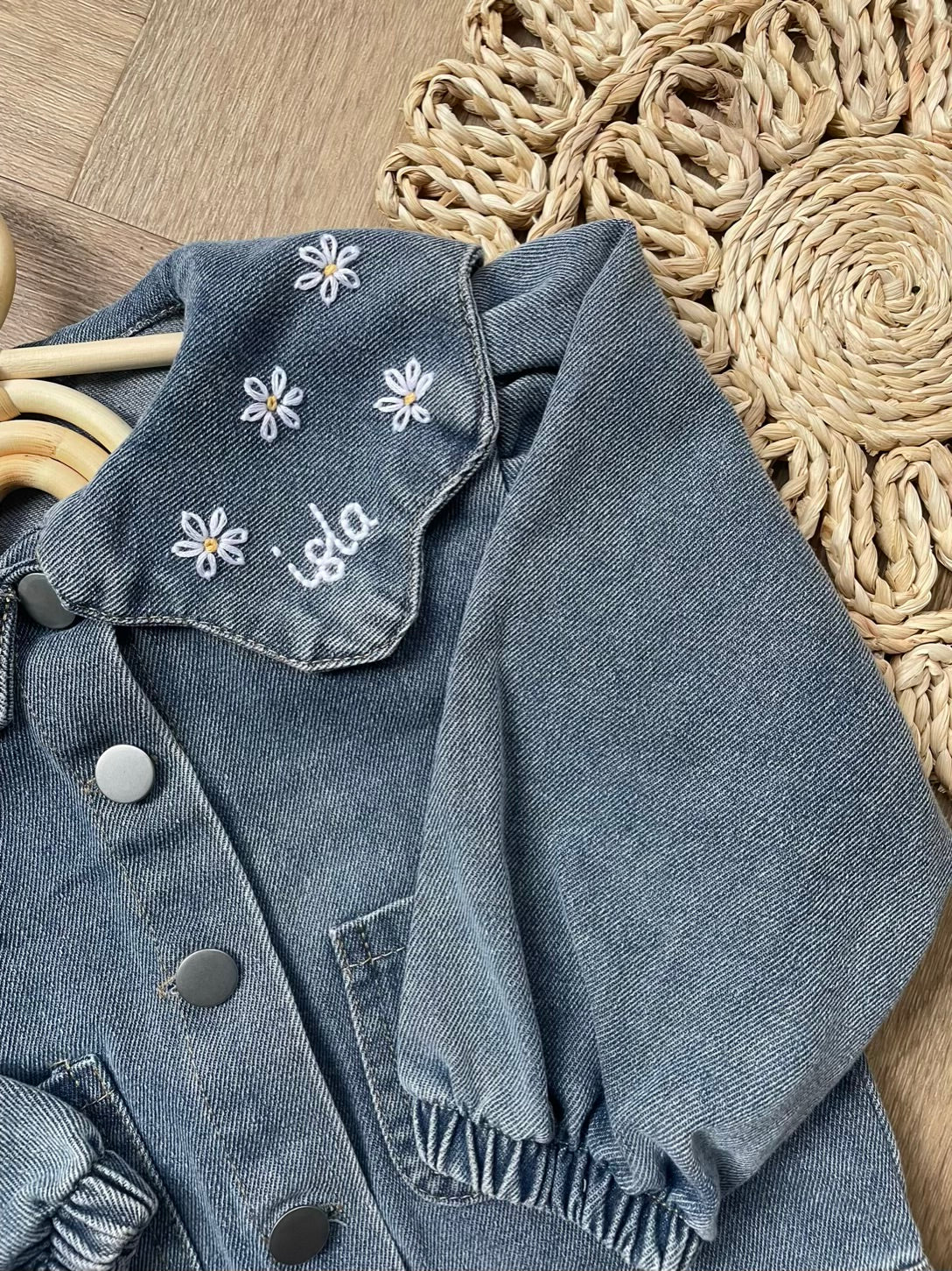 Blue denim jacket with floral embroidery on a textured surface