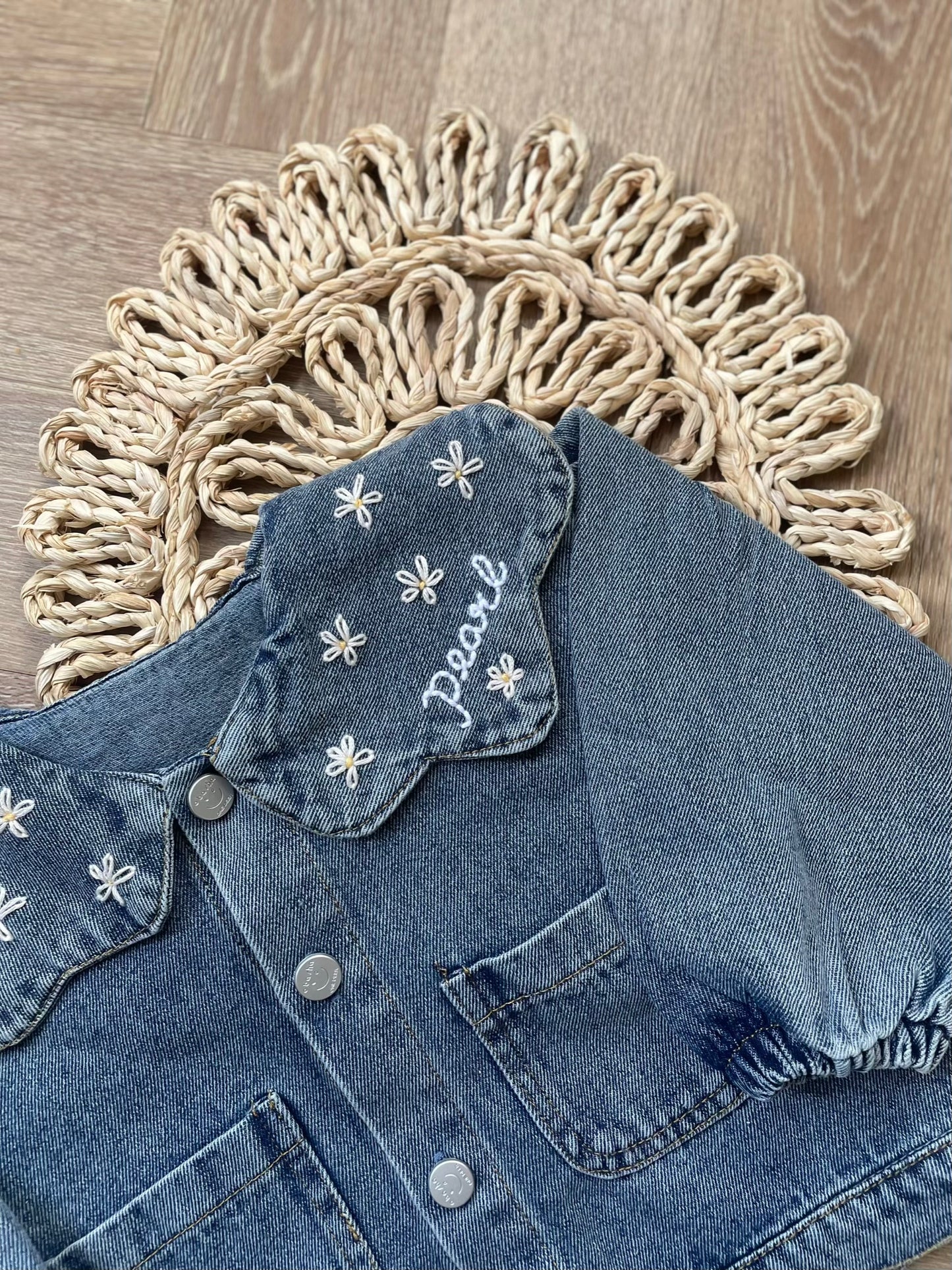 Blue denim jacket with floral embroidery on a textured surface