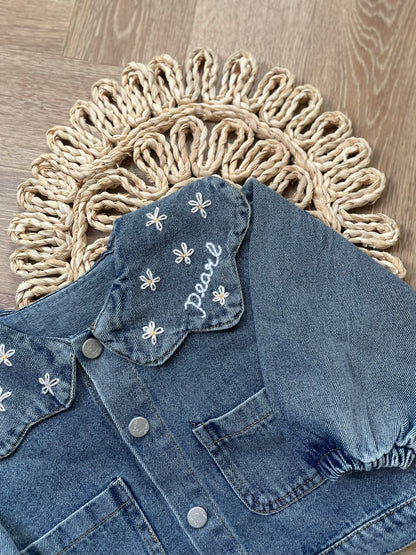 Blue denim jacket with floral embroidery on a textured surface