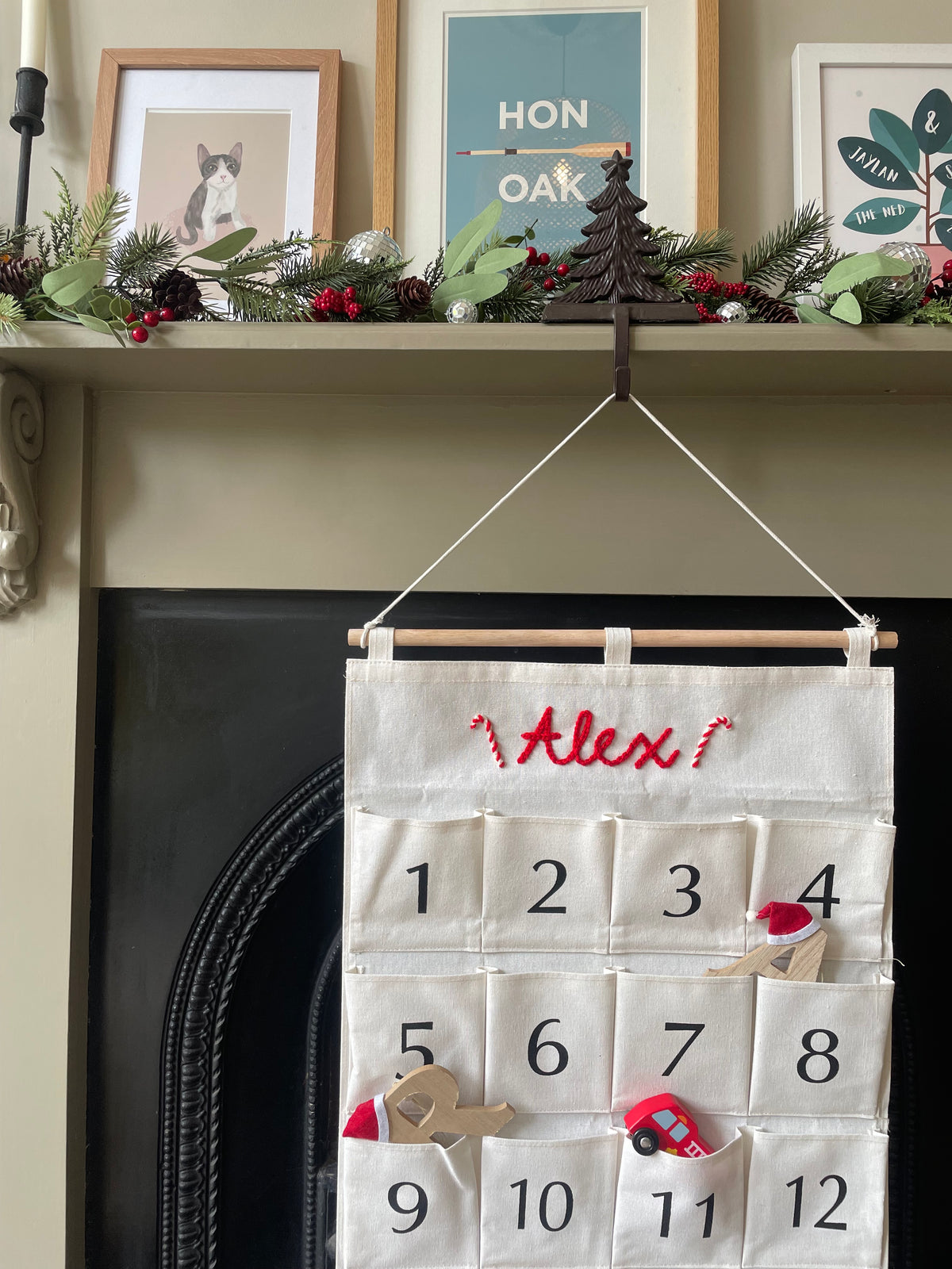 Two personalized Christmas advent calendars laid out on a patterned rug over a wood floor. One calendar is white with the name 'George' in red script and the other is white with the name 'Ruby' in red script, both with numbered pockets and wooden dowels