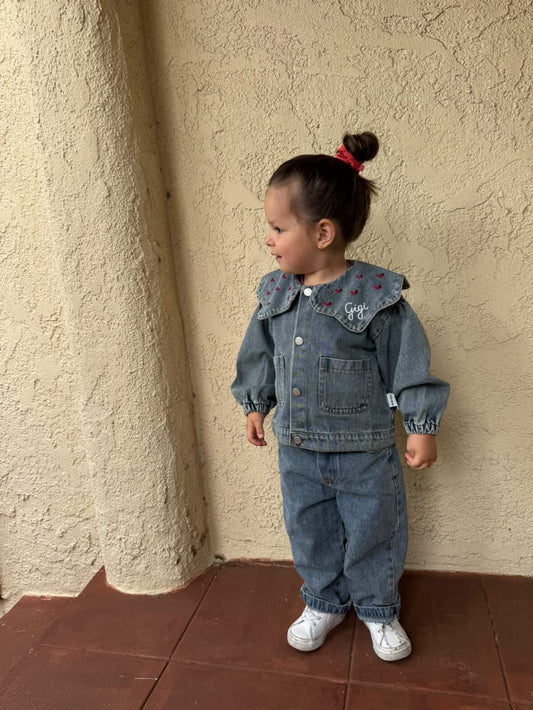 Child wearing a denim outfit standing against a beige wall.